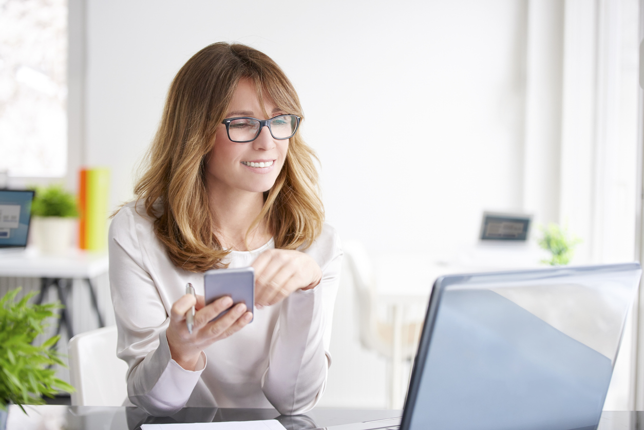Automate your finances- Businesswoman using mobile phone and laptop for investment automation.