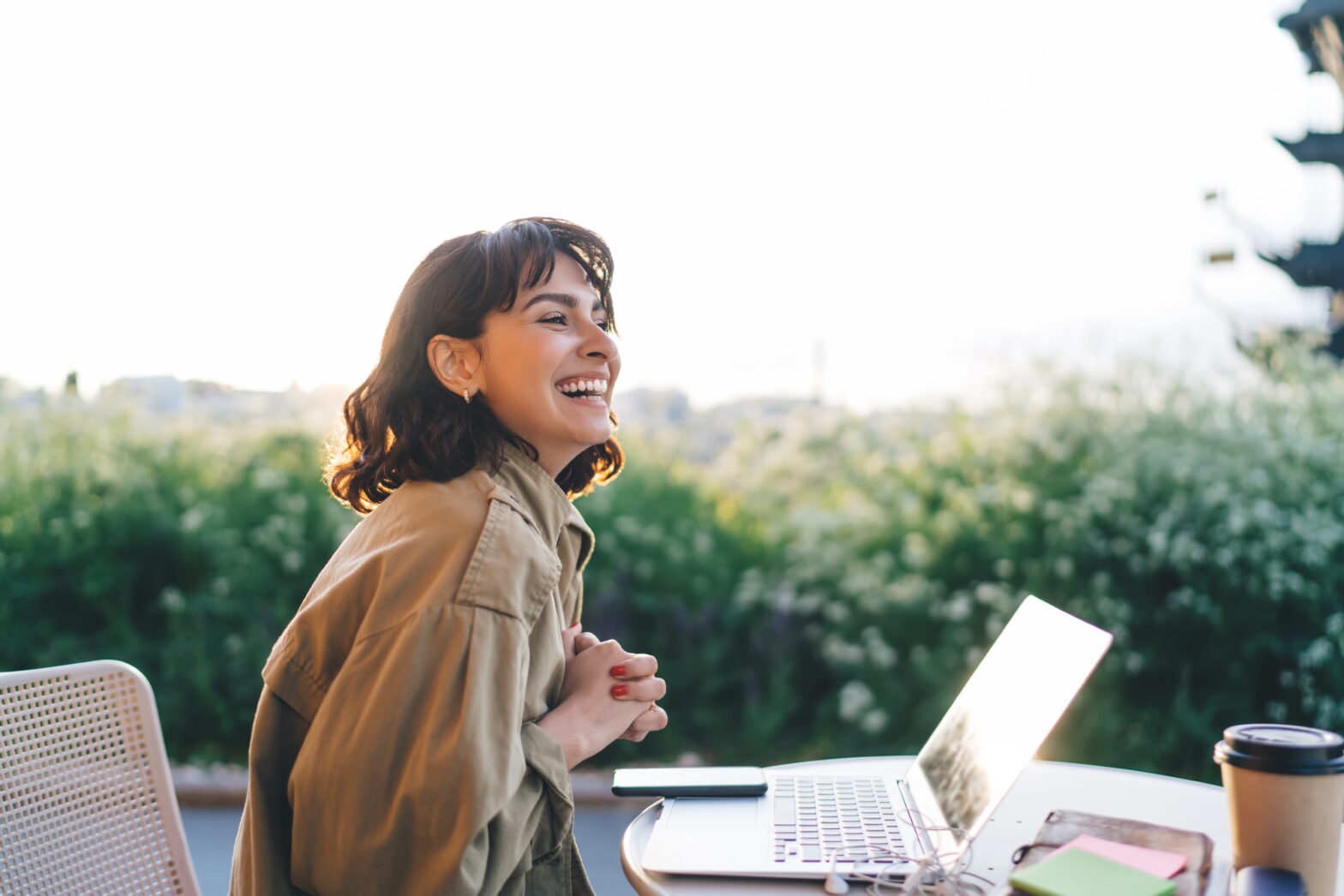 Woman sitting outdoors with a laptop, smiling thoughtfully, representing financial planning and independence after divorce later in life.