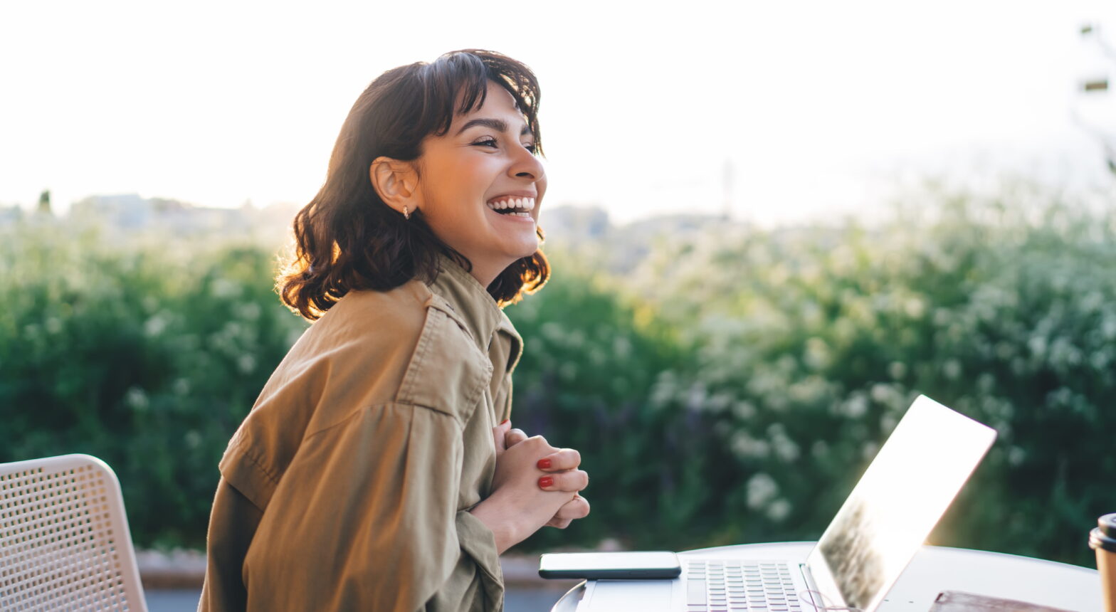 Woman sitting outdoors with a laptop, smiling thoughtfully, representing financial planning and independence after divorce later in life.
