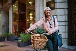 Woman walking a bicycle through a city street, smiling, representing long-term planning, independence, and lifestyle-focused financial decisions.