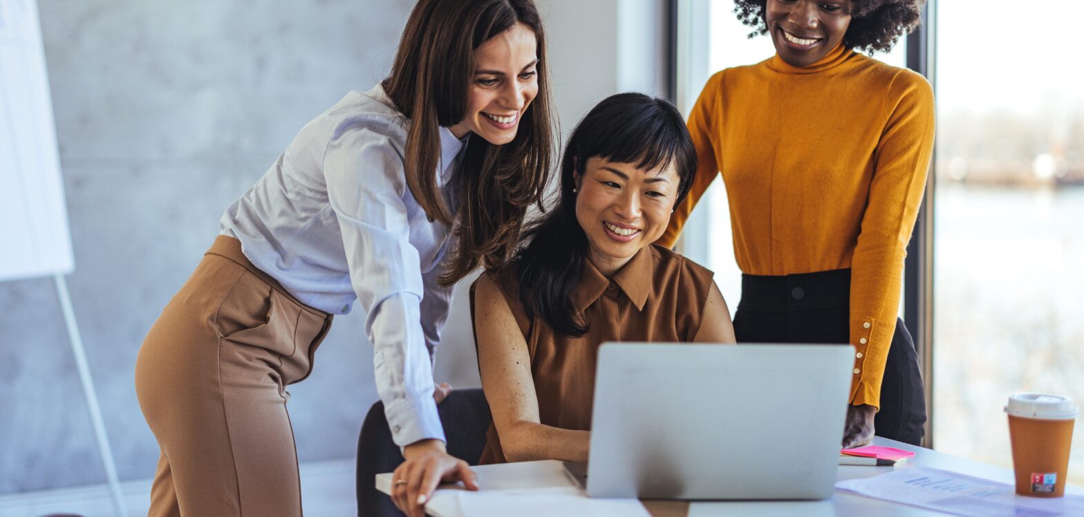 three women looking at one laptop screen in an office environment