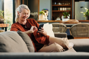 A woman wearing a rust-colored top, smiles while looking at her smartphone while spring cleaning her finances