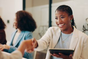 A successful woman shaking another woman's hand after investing while smiling and holding a tablet