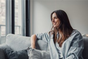A wealthy-minded woman sitting on a couch, looking out the window in thought.